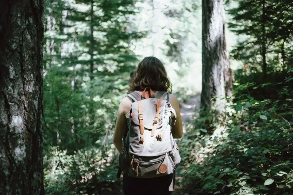 Woman walking with backpack in dense woods.
