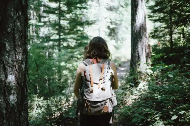 Woman walking with backpack in dense woods.