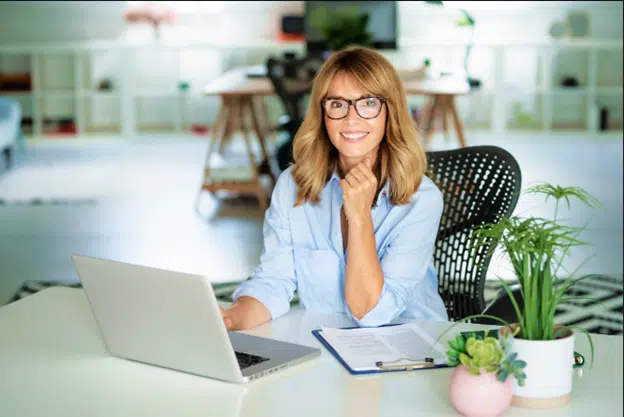 Woman confidently smiling behind her laptop after learning how to boost her self-love and confidence.