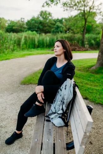 Dr. Stephanie Grunewald of Ancorio sitting on a park bench in an outdoor setting, dressed in athletic wear, with a backpack beside her, gazing into the distance.