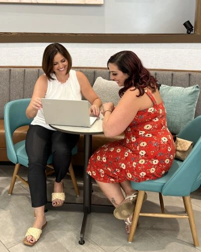 Dr. Stephanie Grunewald of Ancorio sitting at a table with a client, smiling while reviewing something on a laptop in a welcoming, modern space.