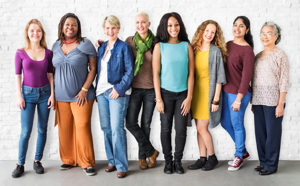 A diverse group of women in The Aligned Entrepreneur mastermind group by Ancorio, standing together and smiling in front of a white brick wall.