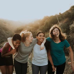 4 women laughing, with arms over each other's shoulders, hiking at a RESET Retreat