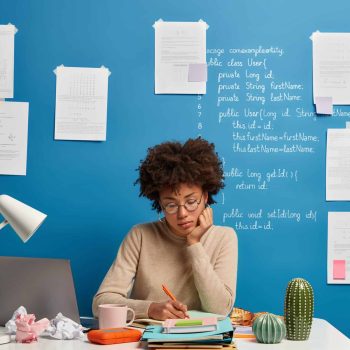 Woman makes notes in notepad surrounded by pile of notebooks.